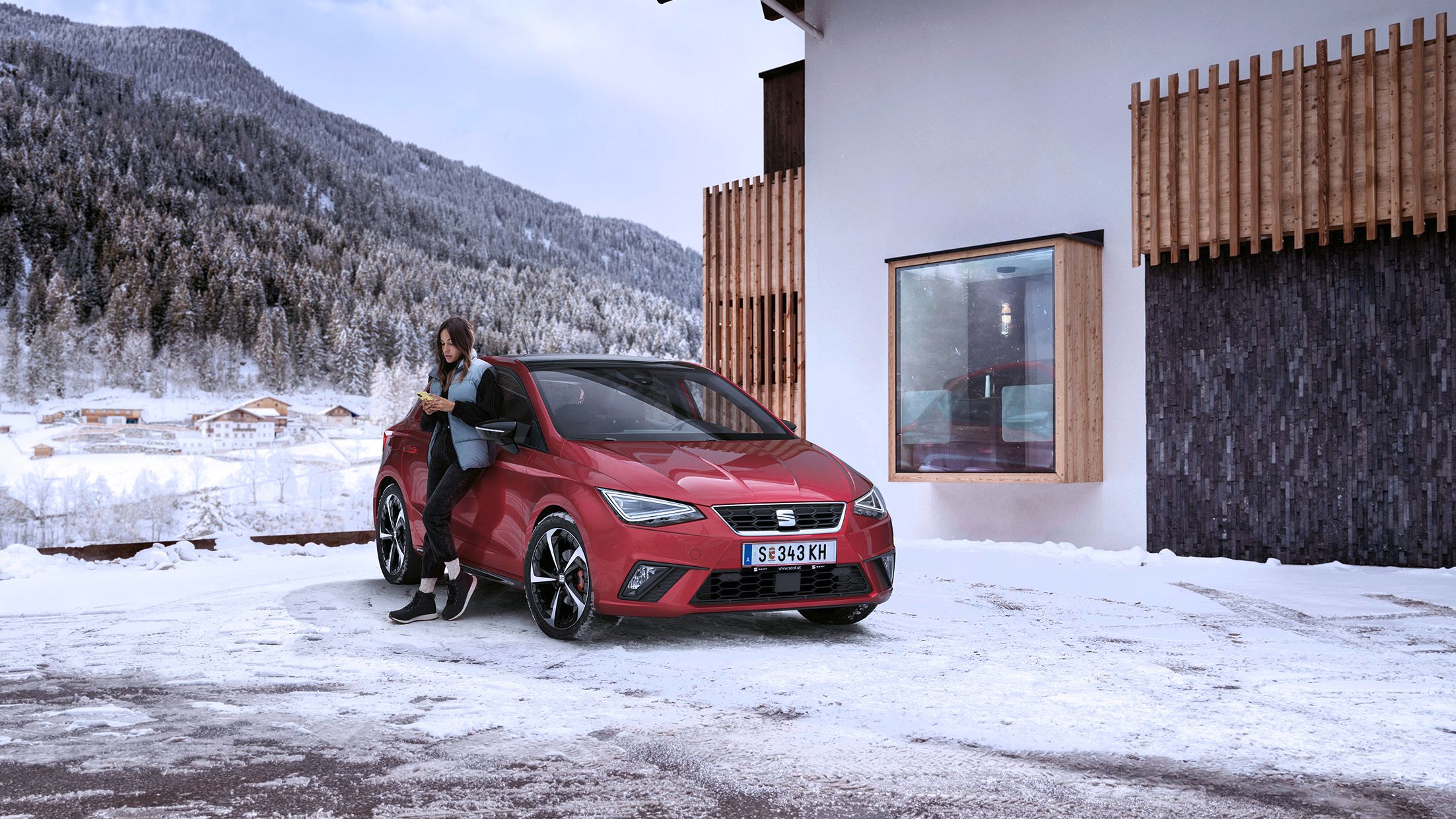 Eine Frau hält ihr Smartphone in der Hand und lehnt an einem roten SEAT Ibiza