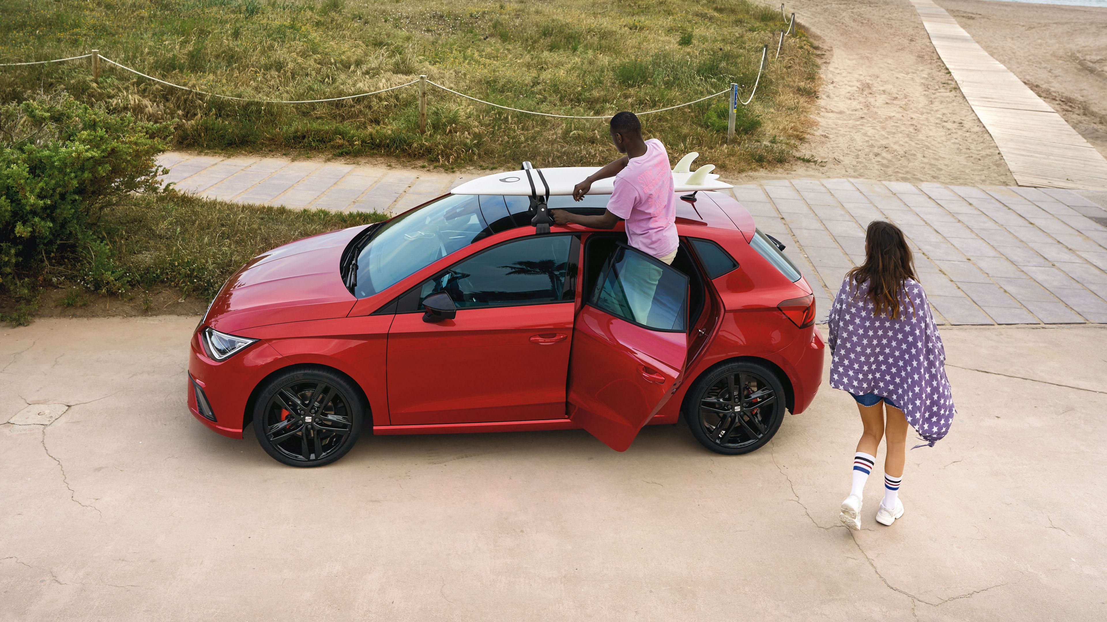 Am Strand ist ein roter SEAT Ibiza geparkt, auf dessen Dach ein Surfbrett montiert ist